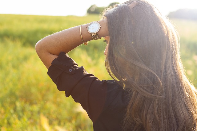 אישה מדגמנת שעון וצמיד עם שדה ברקע
